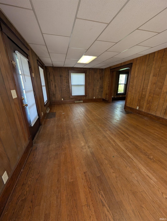spare room featuring wood-type flooring, wooden walls, baseboards, and a drop ceiling