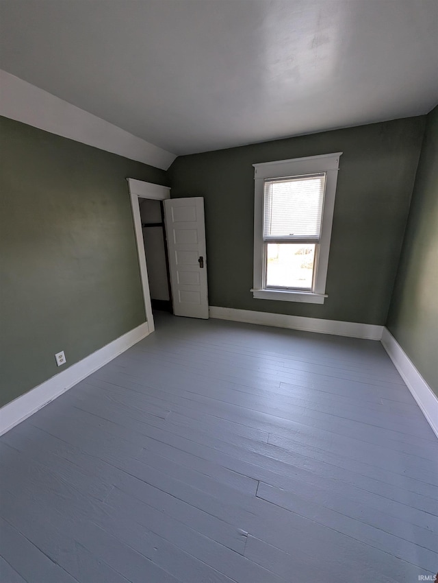 unfurnished room featuring vaulted ceiling, wood finished floors, and baseboards