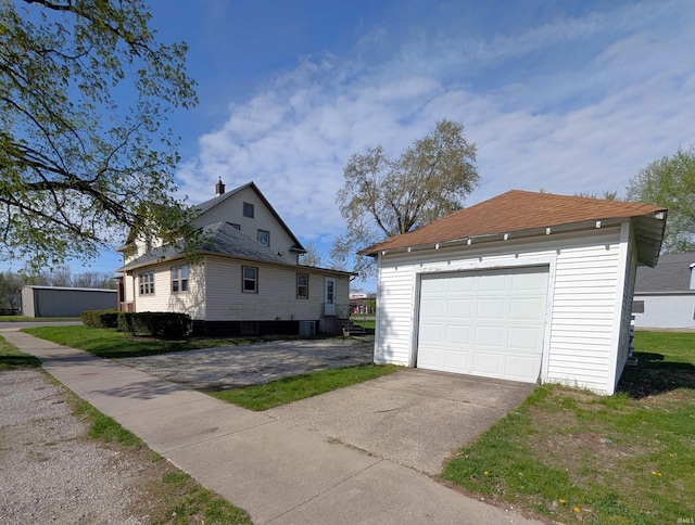 view of home's exterior featuring an outbuilding, a garage, driveway, central AC unit, and roof with shingles