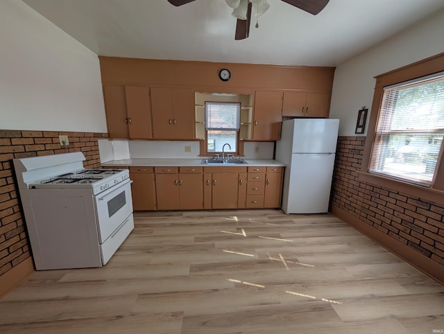 kitchen featuring white appliances, a sink, ceiling fan, brick wall, and light wood finished floors
