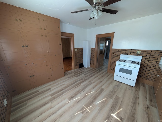 kitchen featuring white gas stove, light wood finished floors, wainscoting, and ceiling fan