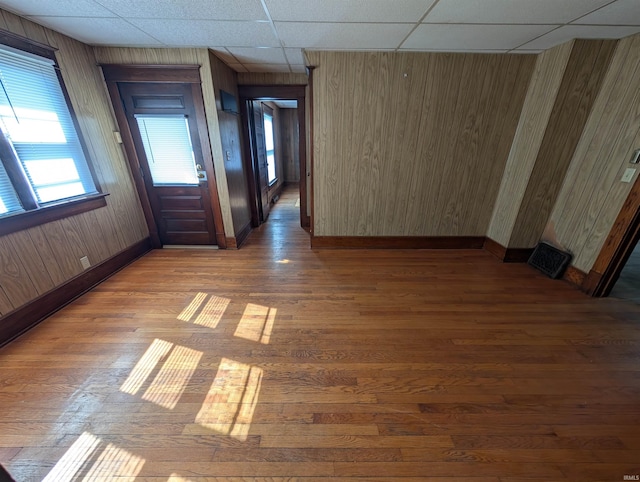unfurnished room featuring wood finished floors, baseboards, a drop ceiling, and wood walls