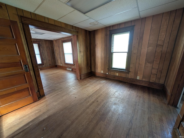 empty room with hardwood / wood-style floors, a paneled ceiling, baseboards, and wooden walls