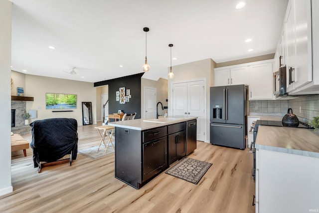 kitchen featuring black fridge with ice dispenser, a sink, light wood-style flooring, dishwasher, and backsplash