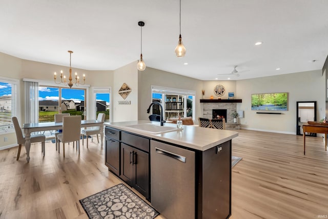 kitchen featuring a sink, dishwasher, a chandelier, a lit fireplace, and light wood finished floors