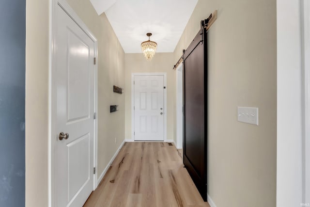 corridor with a barn door, light wood-type flooring, baseboards, and a chandelier