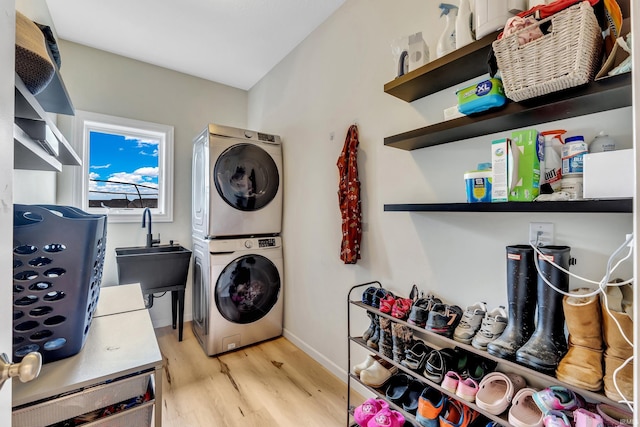 laundry area featuring stacked washer and clothes dryer, light wood finished floors, and baseboards
