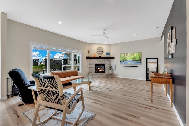 living room featuring light wood finished floors, ceiling fan, baseboards, a stone fireplace, and recessed lighting
