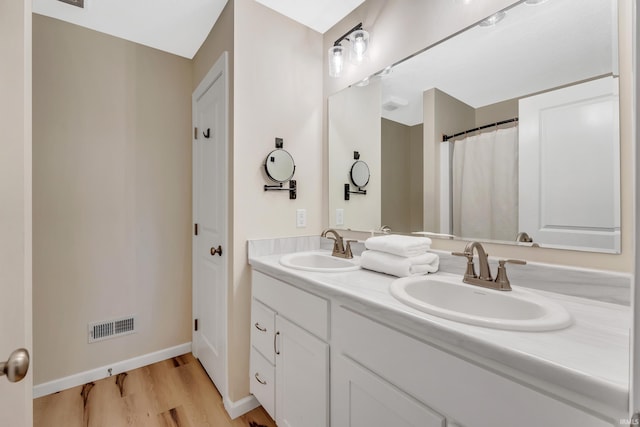 full bath featuring wood finished floors, double vanity, and baseboards