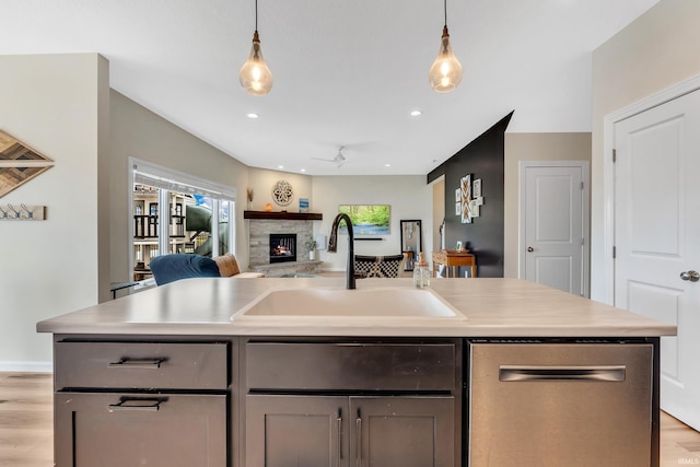 kitchen with stainless steel dishwasher, a sink, light countertops, a fireplace, and light wood-type flooring