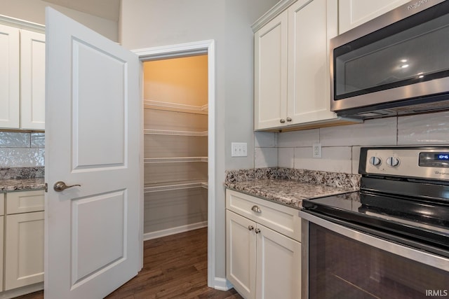 kitchen featuring appliances with stainless steel finishes, white cabinets, dark wood-style flooring, and light stone counters