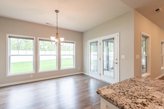 unfurnished dining area featuring healthy amount of natural light, dark wood-type flooring, a chandelier, and baseboards