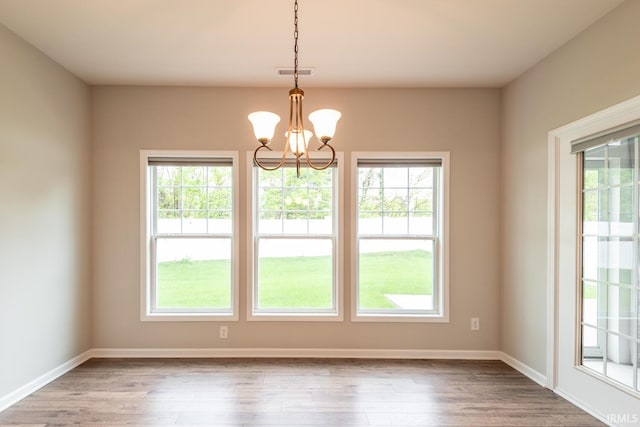 empty room featuring a chandelier, wood finished floors, and baseboards