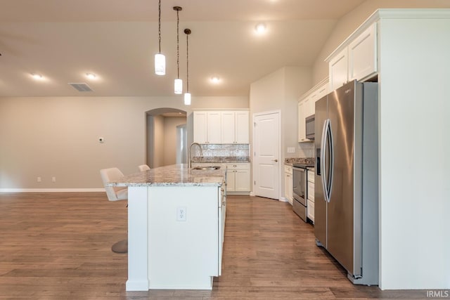 kitchen featuring appliances with stainless steel finishes, arched walkways, a kitchen island with sink, a sink, and dark wood-style floors