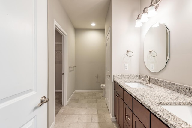 bathroom with toilet, recessed lighting, double vanity, baseboards, and a spacious closet
