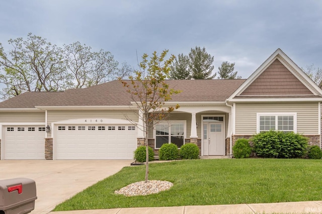 craftsman inspired home featuring a garage, concrete driveway, a front yard, stone siding, and roof with shingles
