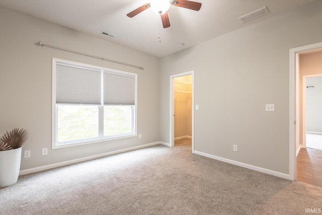 unfurnished bedroom featuring carpet, baseboards, a walk in closet, and ceiling fan