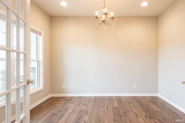 empty room with healthy amount of natural light, a chandelier, wood finished floors, baseboards, and recessed lighting
