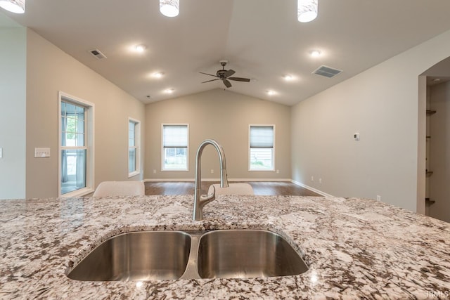 kitchen with open floor plan, a sink, wood finished floors, light stone countertops, and lofted ceiling