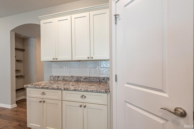 kitchen with arched walkways, baseboards, dark wood finished floors, white cabinets, and light stone counters