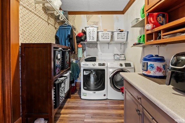 washroom with washing machine and clothes dryer, wallpapered walls, light wood-type flooring, ornamental molding, and a textured ceiling