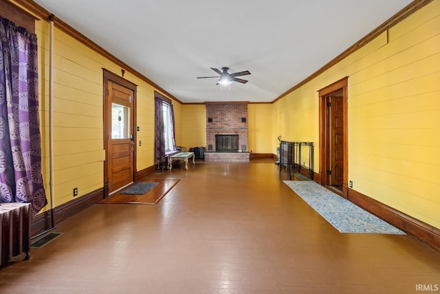 unfurnished living room with crown molding, a ceiling fan, a brick fireplace, baseboards, and wood walls