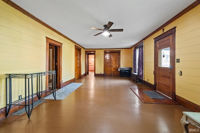 entryway with ornamental molding, a ceiling fan, baseboards, and wooden walls