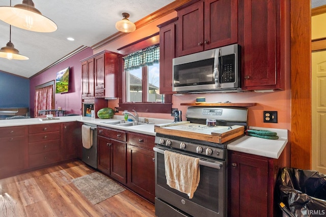kitchen featuring stainless steel appliances, a sink, light countertops, light wood-style floors, and crown molding