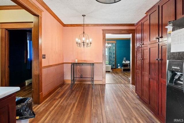 unfurnished dining area featuring wood finished floors, crown molding, radiator heating unit, wainscoting, and a chandelier