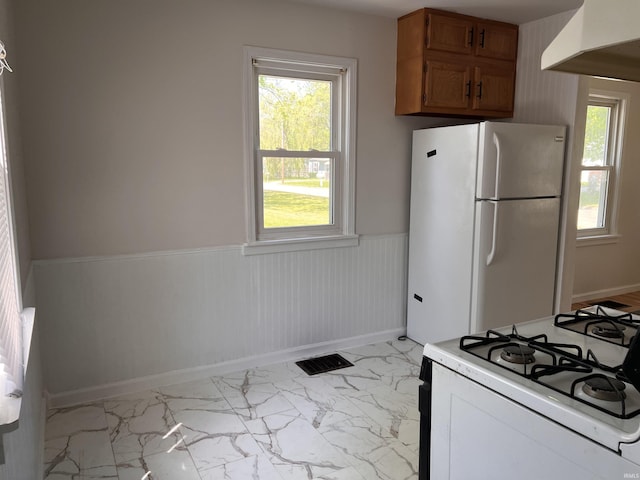 2211 E 19th St, Muncie, IN 47302 - kitchen featuring white appliances, a wainscoted wall, light marble finish flooring, baseboards, and brown cabinets