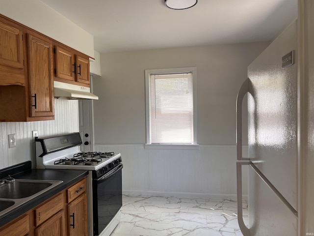 2211 E 19th St, Muncie, IN 47302 - kitchen with under cabinet range hood, range with gas cooktop, light marble finish floors, freestanding refrigerator, and wainscoting