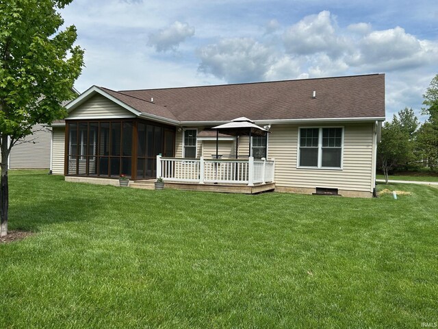 back of property with a deck, a sunroom, a lawn, and a shingled roof