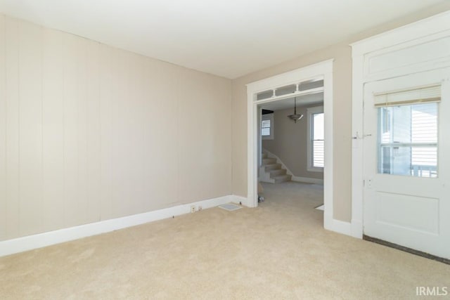 empty room featuring light carpet, stairway, and baseboards