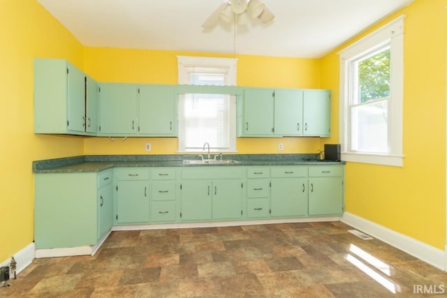 kitchen featuring baseboards, a sink, a ceiling fan, stone finish flooring, and dark countertops