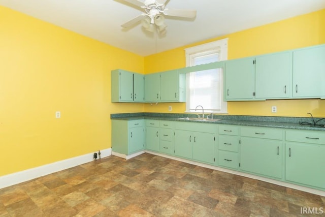 kitchen with a sink, baseboards, a ceiling fan, stone finish floors, and dark countertops
