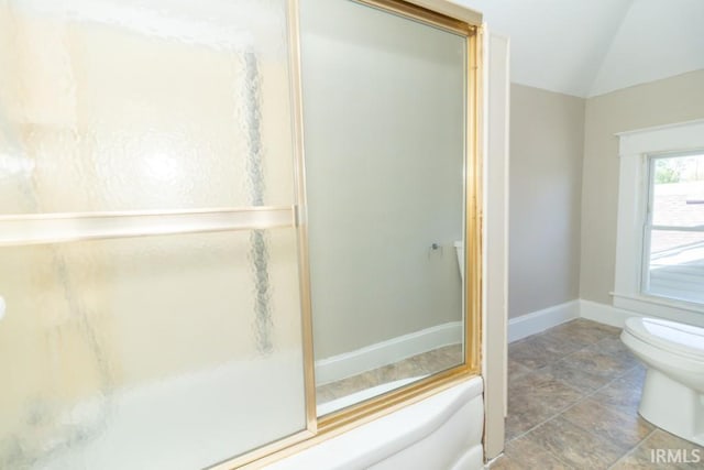 bathroom featuring toilet, baseboards, stone finish floors, vaulted ceiling, and a shower with shower door