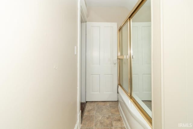 full bathroom featuring stone finish flooring, combined bath / shower with glass door, and baseboards