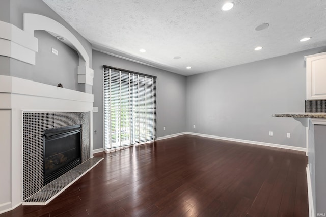2378 The Springs Dr, Indianapolis, IN 46260 - unfurnished living room with a textured ceiling, a tiled fireplace, dark wood-type flooring, recessed lighting, and baseboards