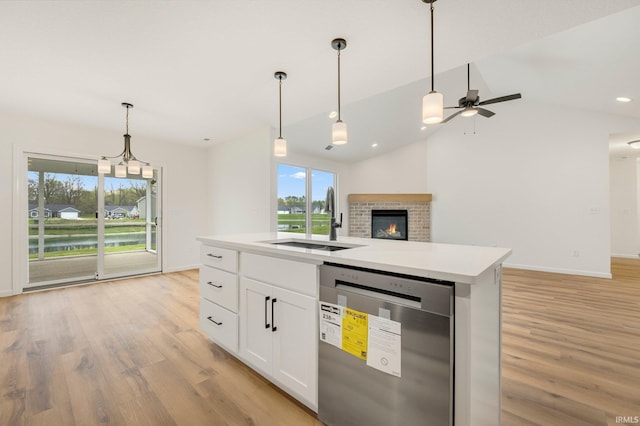 kitchen with stainless steel dishwasher, a sink, open floor plan, light wood-type flooring, and vaulted ceiling