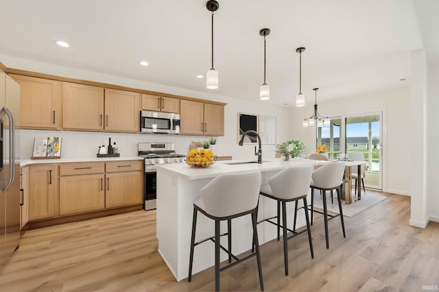 kitchen with stainless steel appliances, a sink, light countertops, a breakfast bar, and light wood-type flooring