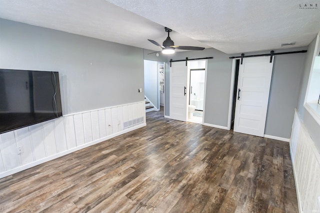 unfurnished living room featuring a barn door, wood finished floors, ceiling fan, a textured ceiling, and baseboards