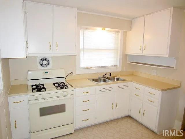 kitchen featuring white range with gas cooktop, a sink, light countertops, and white cabinetry