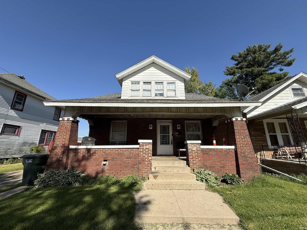 view of front of home with brick siding, covered porch, and roof with shingles