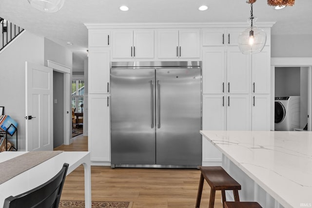 kitchen with built in refrigerator, washer / dryer, light wood-style flooring, white cabinets, and light stone countertops