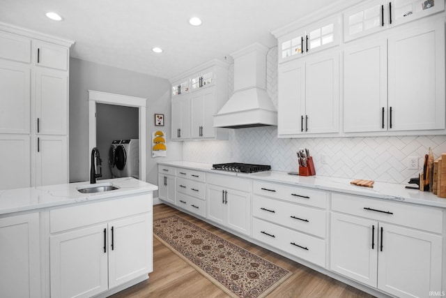 kitchen featuring custom range hood, separate washer and dryer, a sink, gas stovetop, and decorative backsplash