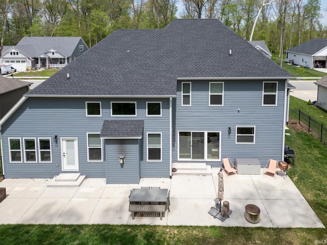 rear view of house with entry steps, a patio, fence, and roof with shingles
