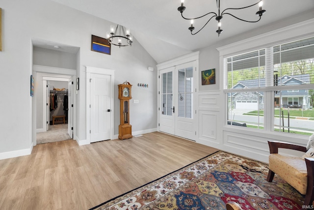 entrance foyer with a chandelier, vaulted ceiling, light wood-style floors, and baseboards