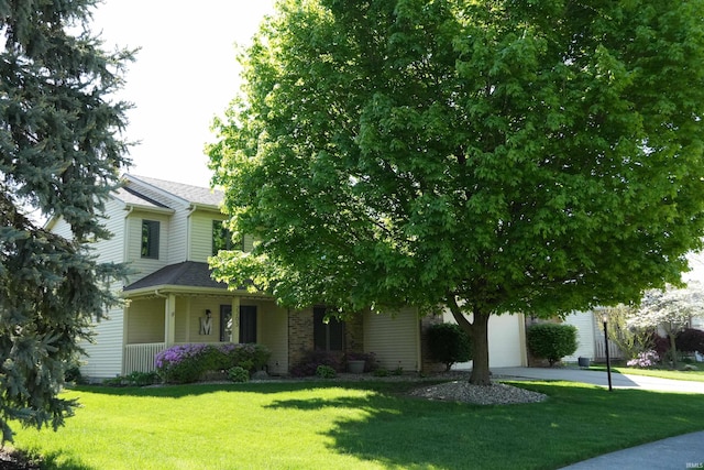 view of front of property with a front yard, covered porch, a shingled roof, and concrete driveway