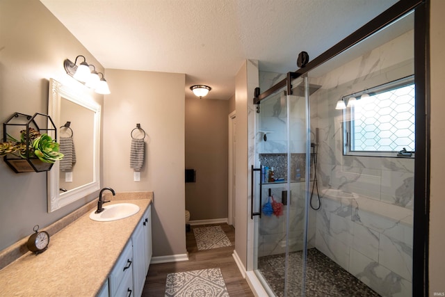 full bathroom featuring a marble finish shower, vanity, a textured ceiling, toilet, and wood finished floors