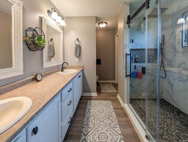 bathroom featuring double vanity, a shower stall, wood finished floors, toilet, and baseboards